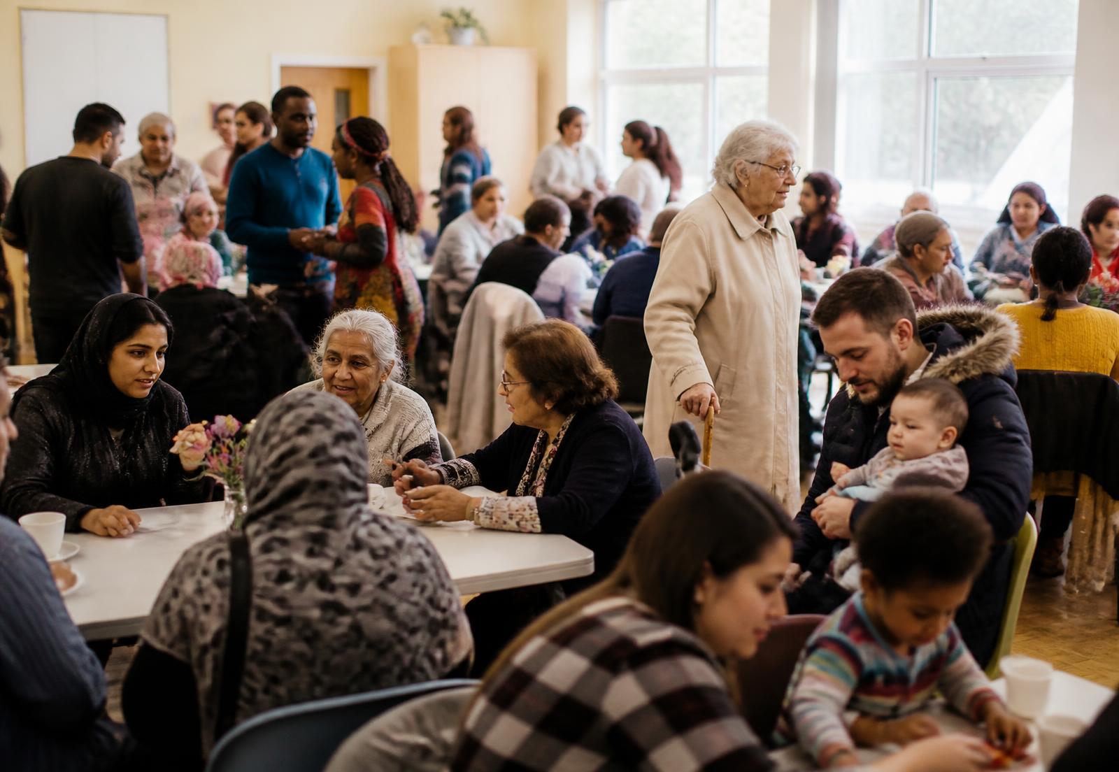 A busy multicultural community gathering with people of all ages sharing tea and conversation