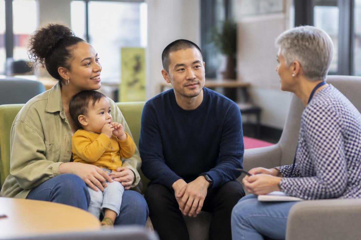 A mixed-heritage family with a toddler talking with a family support worker in a community centre